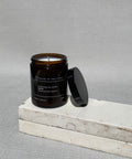 Calm soy candle by house of two trees, amber glass jar with a black lid and a cream label