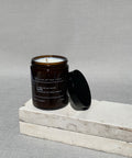 Earth soy candle by house of two trees, amber glass jar with a black lid and a cream label